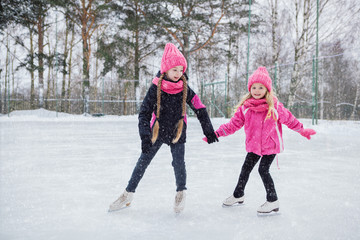 Fototapeta na wymiar Two Little smiling girls skating on ice in pink wear.