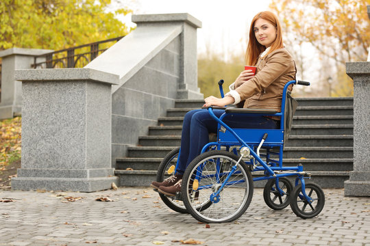 Young woman in wheelchair with cup of coffee outdoors