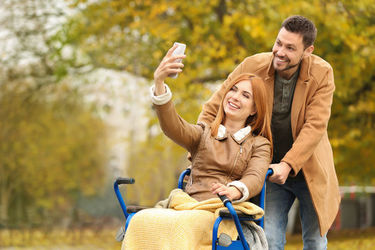 Young woman in wheelchair and her husband taking selfie outdoors