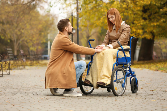 Young woman in wheelchair and her husband outdoors on autumn day
