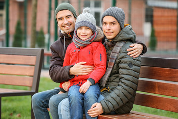 Male gay couple with adopted boy sitting on bench in park