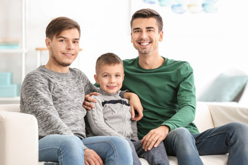 Male gay couple with adopted boy sitting on sofa at home