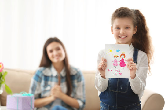 Cute little girl holding greeting card for her mom indoors. Mother's day celebration