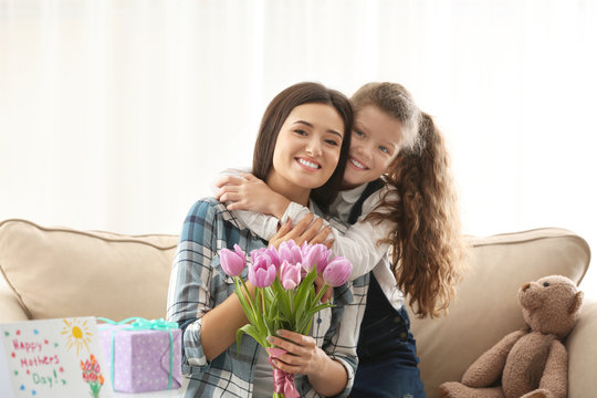 Young woman and her daughter with tulip bouquet indoors. Mother's day celebration