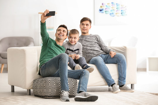 Male gay couple with adopted boy taking selfie at home