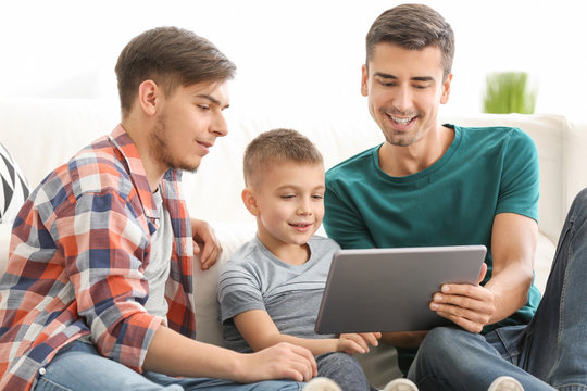 Male gay couple and adopted boy with tablet at home