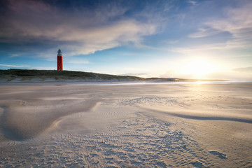 sunset behind red lighthouse on sea coast