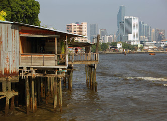 Bangkok, Thailand - 04 11 2017: Ancient wooden Construction on Poles at the Chao Praya River, modern High Rises in Background © christianthiel.net