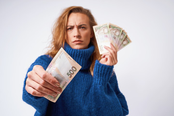 A frustrated girl in a sweater holding money, on a gray background.