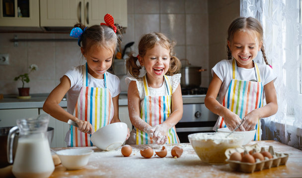 happy sisters children girls bake cookies, knead dough, play with flour and laugh  .