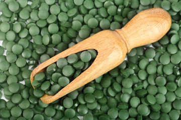heap of Spirulina tablets algae nutritional supplement in wooden scoop as a background close up top view. Flat lay
