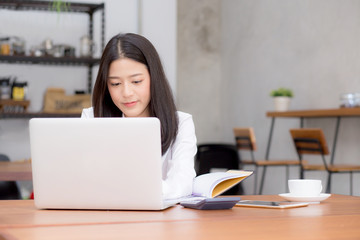 Fototapeta premium Beautiful asian young woman working online on laptop sitting at coffee shop, professional female freelancer using notebook computer with connect to internet for distance job.