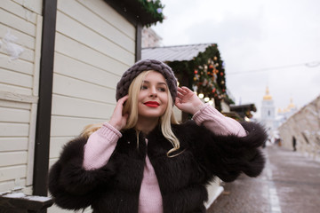 Street portrait of stylish young woman wearing stylish knitted hat and fur coat, posing at the...