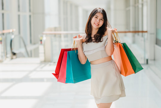 Happy Asian beautiful woman enjoying and smiling with colorful shopping bag in her both hand in mall.