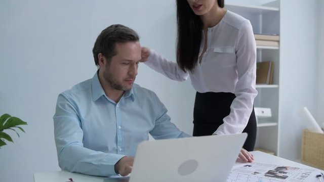 Office flirt. Young woman bringing her busy chief a cup of tea and touching his shoulders before doing a back message for him.