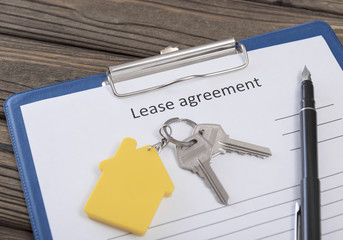 form of the lease agreement, two keys from the front door on a key fob in the form of a house on the background of a wooden table. business. Sew housing. the lessor. profit.