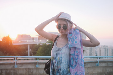 Beautiful young pretty casual fashion lady with a pink hat on roof top having relax time. Cute cheerful girl sitting on the roof with view on the city. Freedom hippie concept.