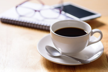 Cup of hot coffee with book, glasses and mobile phone on working day
