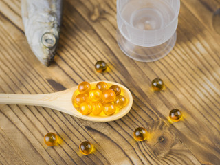 Fish oil pills in a wooden spoon on the table and fish in the background. Traditional medicine.