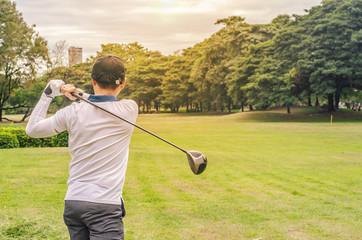 golf player hitting shot with club on course at beautiful morning with sun flare in background
