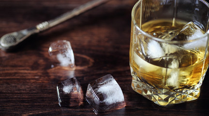 Whiskey with ice with a glass. Cubes of ice on a wooden table an