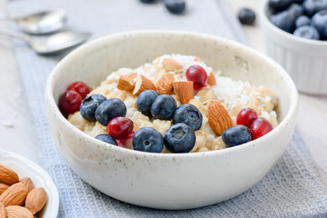 Oatmeal porridge with blueberries, cranberries and almonds in white bowl. Closeup view. Concept of healthy eating, dieting, healthy lifestyle
