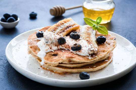 Oat pancakes with greek yogurt, roasted banana, blueberries and cinnamon on white plate