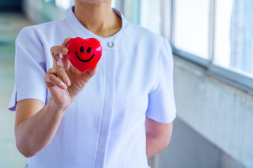 A nurse holding red heart toy. She is Left / right hand holding it.The photo shows the principle of caring and good health.