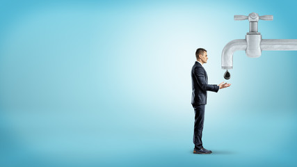 Obraz premium A tiny businessman stands near a giant metal faucet and holds out his hands to catch a giant oil drop.