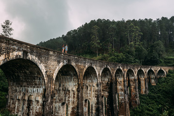 Loving couple on the edge of the bridge. Guy and girl traveling around Asia. The couple travels to Sri Lanka. Man and woman in an unusual place. Nine-arch bridge. Travellers in Asia. Hold hands