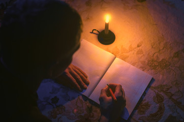 Man is studing and writes in a notebook by lies on the floor in the light of candle. Person writes...