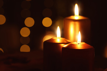 Fototapeta na wymiar Beautiful burning candles in darkness against defocused lights