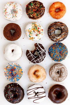 assorted donuts with chocolate frosted, white glazed and sprinkled donuts on white background, top view