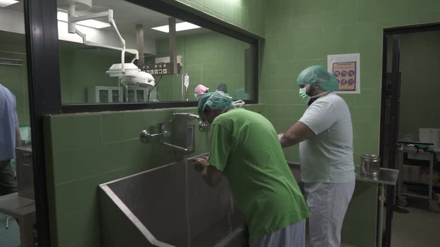 Portrait of surgeons in protective gown, mask, cap and gloves washing hands before surgical operation at washroom in front of operating theater, steadicam, motion to wide angle view, concept surgery.