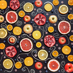 Colorful fruit pattern of fresh orange, apple, pomegranate, blueberry, persimmon, mandarin, cranberry and grapefruit slices on black background. Top view