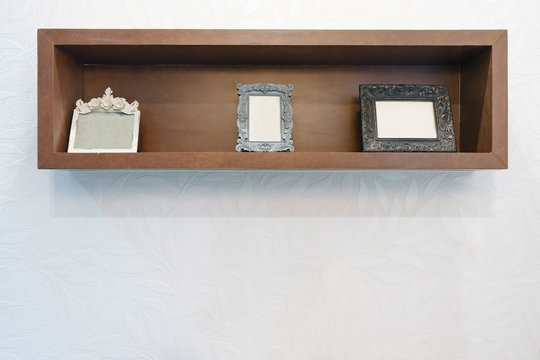 Empty photo frame on wooden shelf with white wall background