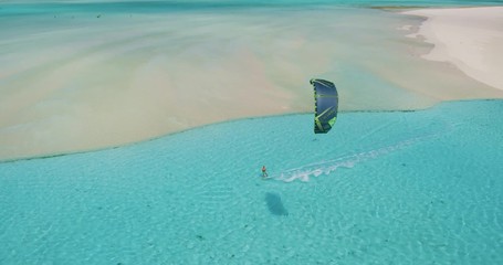Cinematic aerial view of kiteboarder gliding across tropical ocean