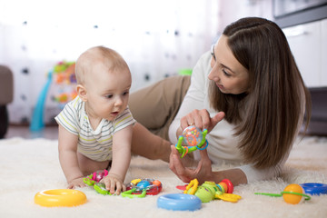 Obraz na płótnie Canvas Adorable baby and young woman playing in nursery. Happy family having fun with colorful toy at home.