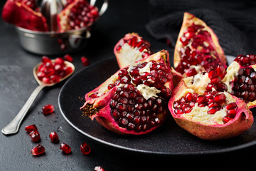 Fresh ripe pomegranate, cut into pieces on black concrete or stone background. Selective focus. Place for text.