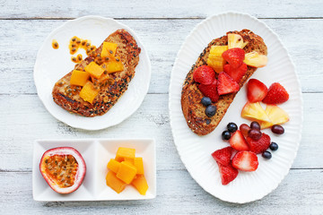 Closeup of french toasts with fresh strawberry, pineapple, grape, mango, passion fruit and orange on white table. Top view of healthy breakfast or brunch.