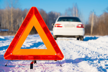 warning triangle and white car on winter snowy country road, focus on triangle, down view point