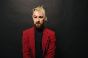 Indoor shot of handsome blond beard male with calm expression, dressed in fashionable jacket, remember something, black background with copy space for your promotional text