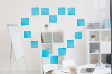 Heart made up of blue notepapers on transparent board in office
