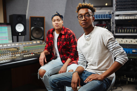 Two African-american producers sitting in audio studio and looking at camera
