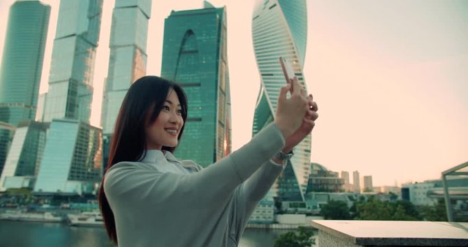 beautiful girl Asian model is making a selfie on the background of skyscrapers using a smartphone