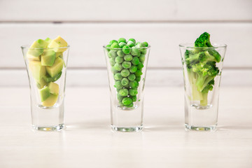 Assortment of green cut vegetables in shot glass on white background.