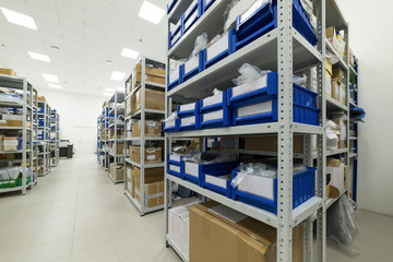 Obraz premium Industrial warehouse. White metal racks with blue plastic trays and cardboard boxes installed in them.