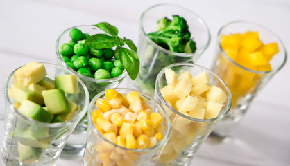 Assortment of yellow and green cut vegetables in shot glass on white background.