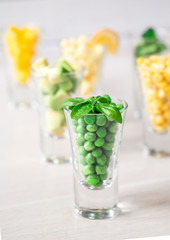 Assortment of yellow and green cut vegetables in shot glass on white background.