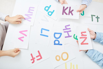 Hands of kids holding paper cards with colorful letters during alphabet play